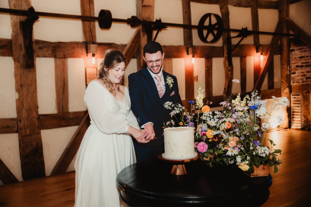 Cake cutting moment with a rustic buttercream cake decorated with fresh flowers at Barns and Yard