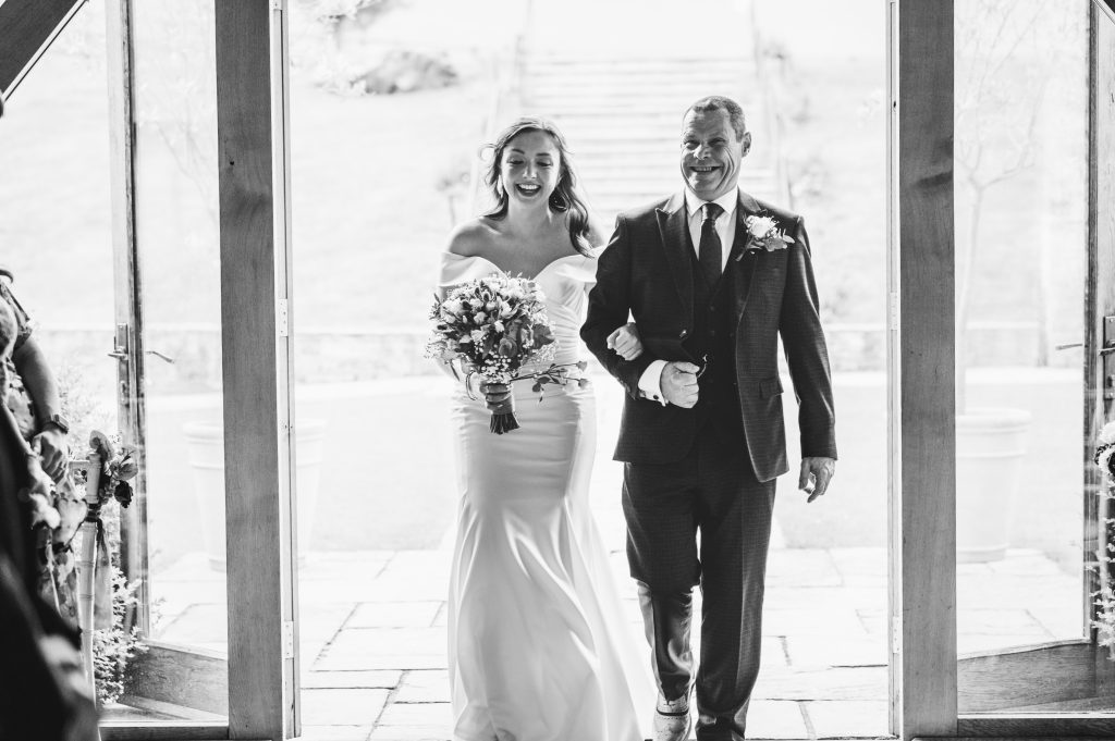 Bride walking down the aisle with her father inside The Barn at Upcote, Cotswold wedding photography