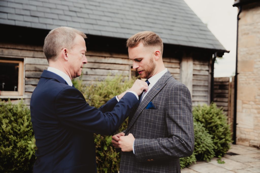 Adjusting tie outdoors at The Barn at Upcote, shot by Gloucestershire wedding photographer