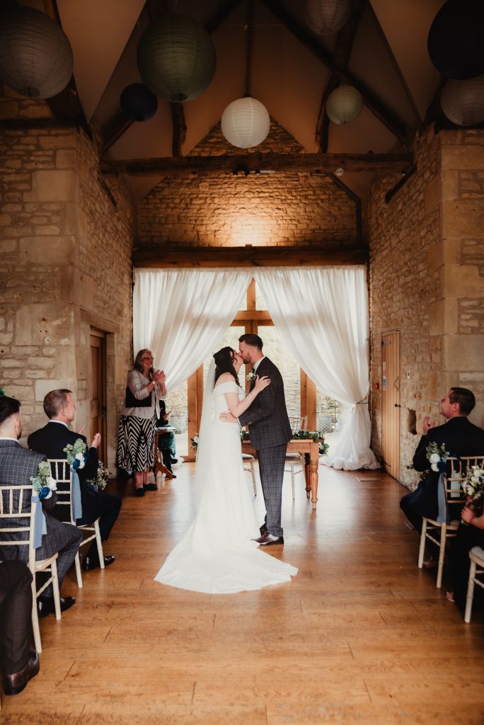 Bride and groom first kiss during their relaxed wedding ceremony, photographed by a Cotswold wedding photographer