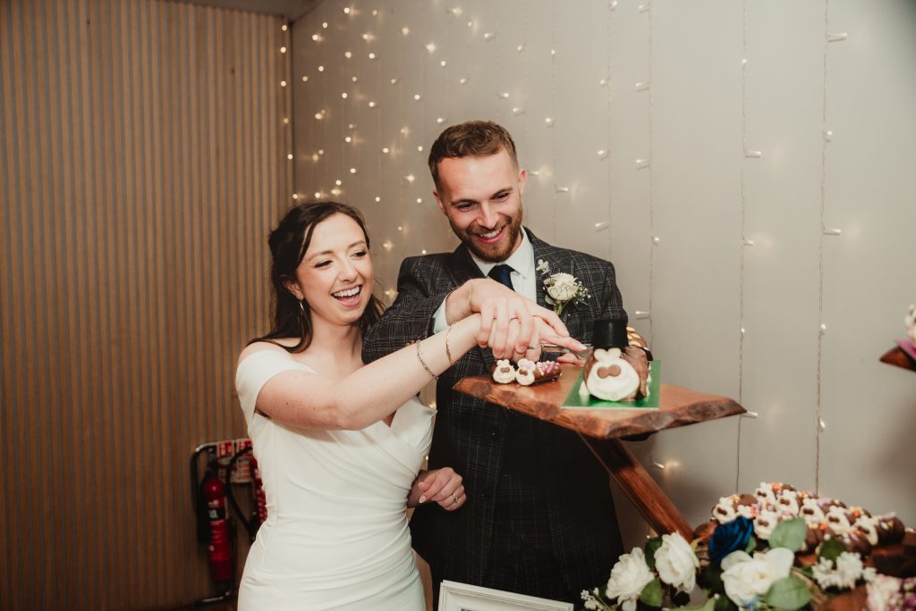 Bride and groom cutting Colin the Caterpillar wedding cake at The Barn at Upcote, Cotswold wedding vibes